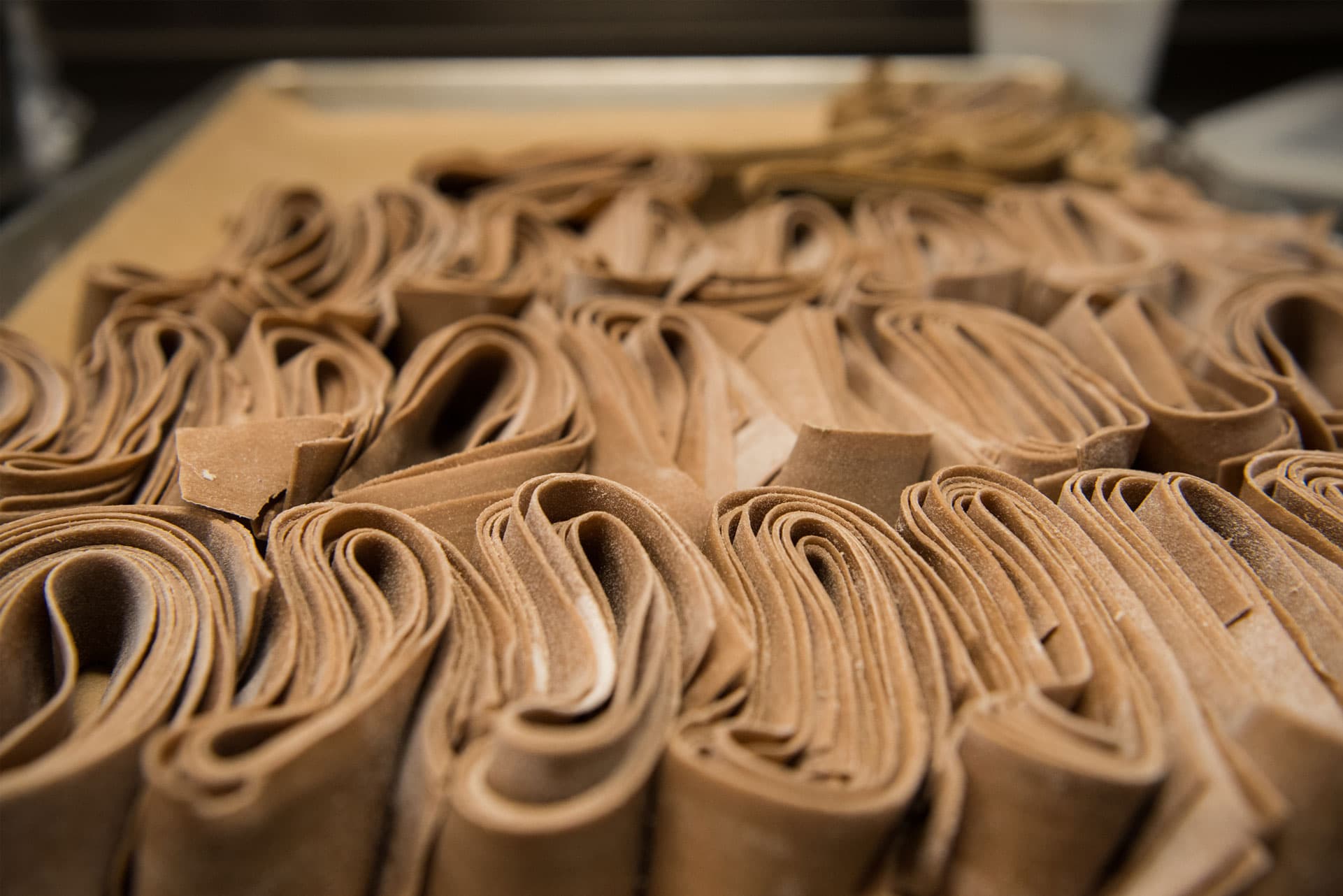 Close-up of folded ribbons of fresh chocolate-brown pasta resting on a floured tray.