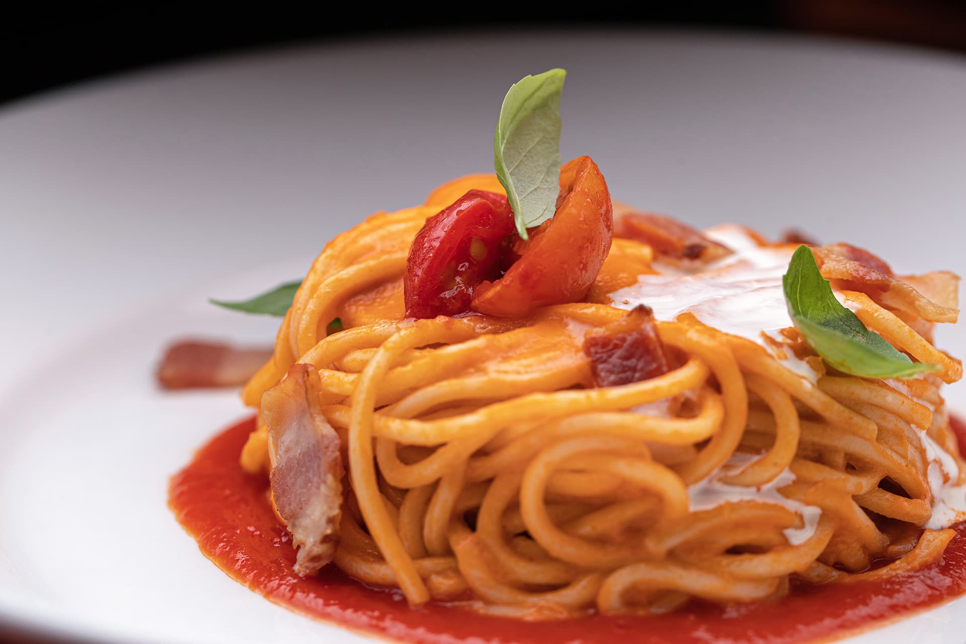 Nest of spaghetti in tomato sauce topped with cherry tomatoes, basil and pancetta.