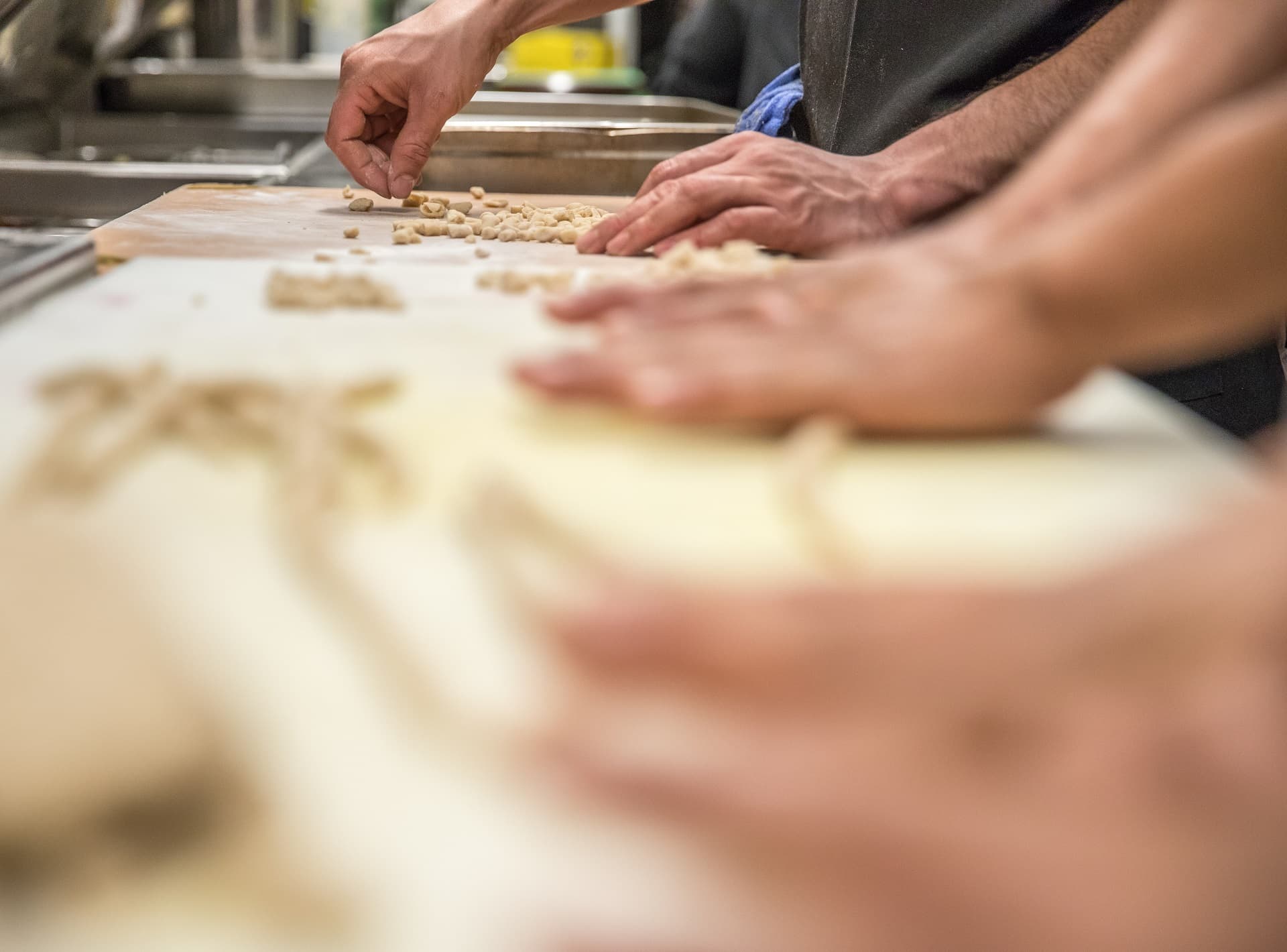 Hands shaping small pieces of fresh pasta dough on a flour-dusted board in a restaurant kitchen.